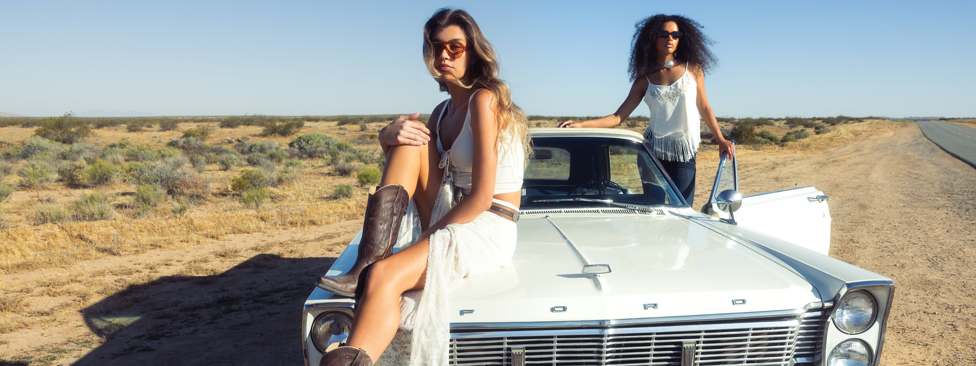 Two women by a vintage Ford car in a desert setting