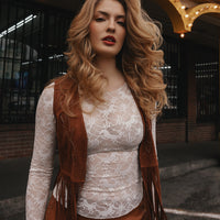 Woman wearing a lace top and brown fringed vest outdoors.