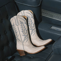 Pair of white cowboy boots with blue embroidery on a car seat.