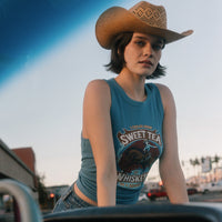 Person wearing a blue tank top with a graphic design and a cowboy hat outdoors.